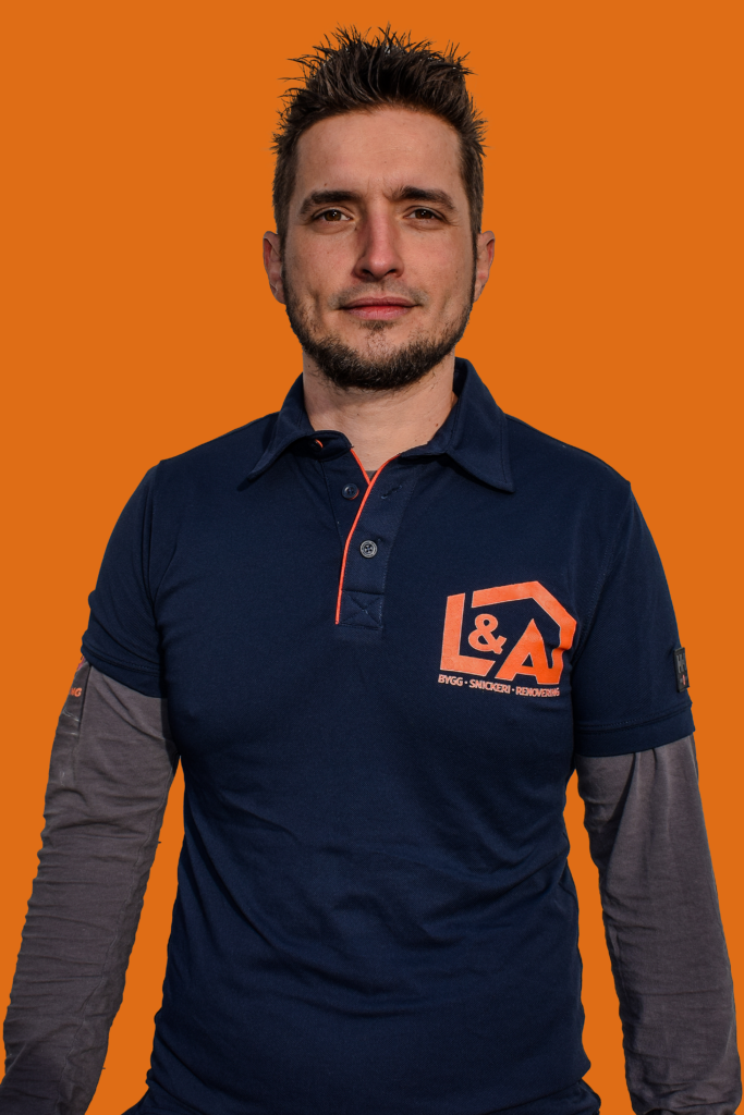 Leszek Sokolowski, en av ägarna till L&A Fantastic Renovering, står framför en orange bakgrund. Han bär en mörkblå pikétröja med företagets logotyp och texten "Bygg - Snickeri - Renovering".
