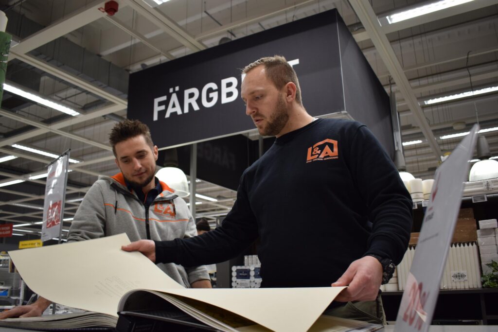 Två av ägarna till L&A Fantastic, ett bygg- och renoveringsföretag i Stockholm, bläddrar i en tapetkatalog i en butik. De står på färg och tapetavdelningen och diskuterar val av material för ett husprojekt i Stockholm.