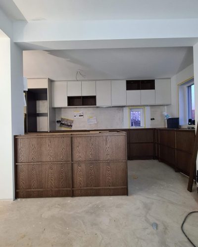 Köksrenovering i Stockholm i ett tidigt skede, med pågående installation av köksö och skåp. Köket har mörka träunderskåp, vita överskåp och en öppen planlösning. Väggarna är förberedda för montering och byggmaterial syns på golvet.