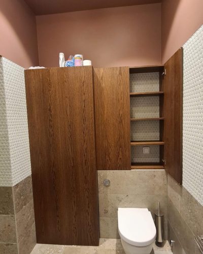 Renoverat badrum med vägghängd toalett, naturstensplattor och rosa målade väggar. Platsbyggd badrumsmöbel i mörkt trä med integrerad förvaring och hexagonmönstrad kakelbakgrund. Badrumsrenovering i Stockholm.