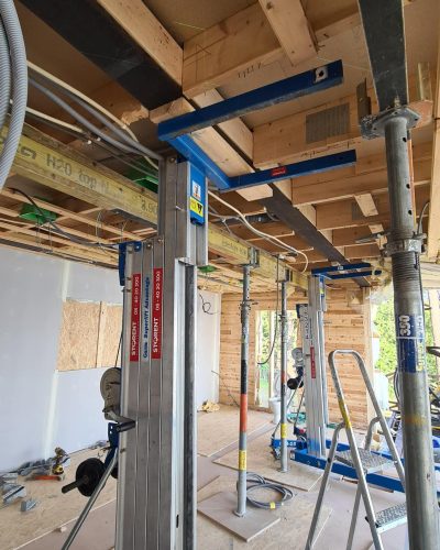 Pågående byggprojekt i Stockholm där taket stöds upp med stöttor. Träkonstruktionen är synlig, med monterade balkar och dragna elkablar. Byggmaterial och verktyg ligger på golvet, och en stege står uppställd i arbetsområdet.