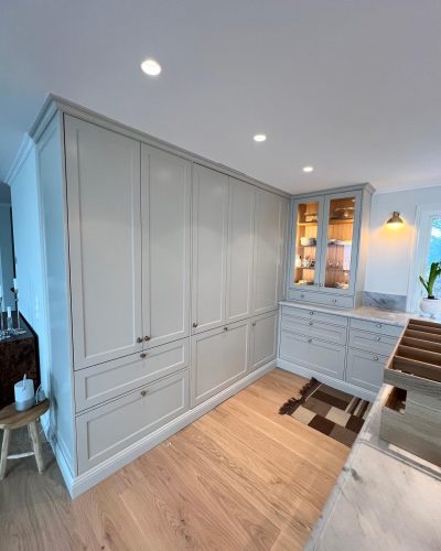 Stilrent nyrenoverat kök med platsbyggda grå skåp som erbjuder gott om förvaring. Vitrinskåp med belysning, marmorbänkskivor och detaljer i trä ger en elegant känsla. Renovering utförd i Stockholm.